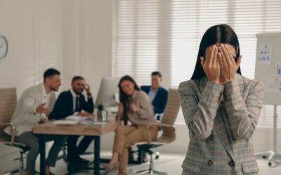 Woman feeling excluded in office while others laugh, symbolizing unfair treatment. Text: "How ‘No Unfair Helping’ Rules Benefit Small Shops | Tech Garcons."