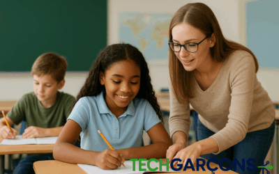 A young female teacher with glasses helps a smiling student with her writing in a classroom, while another student works in the background. The TechGarçons logo is displayed at the bottom of the image